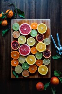 slices of colorful citrus fruit laid on a wooden board beside a lemon press and some fresh fruit