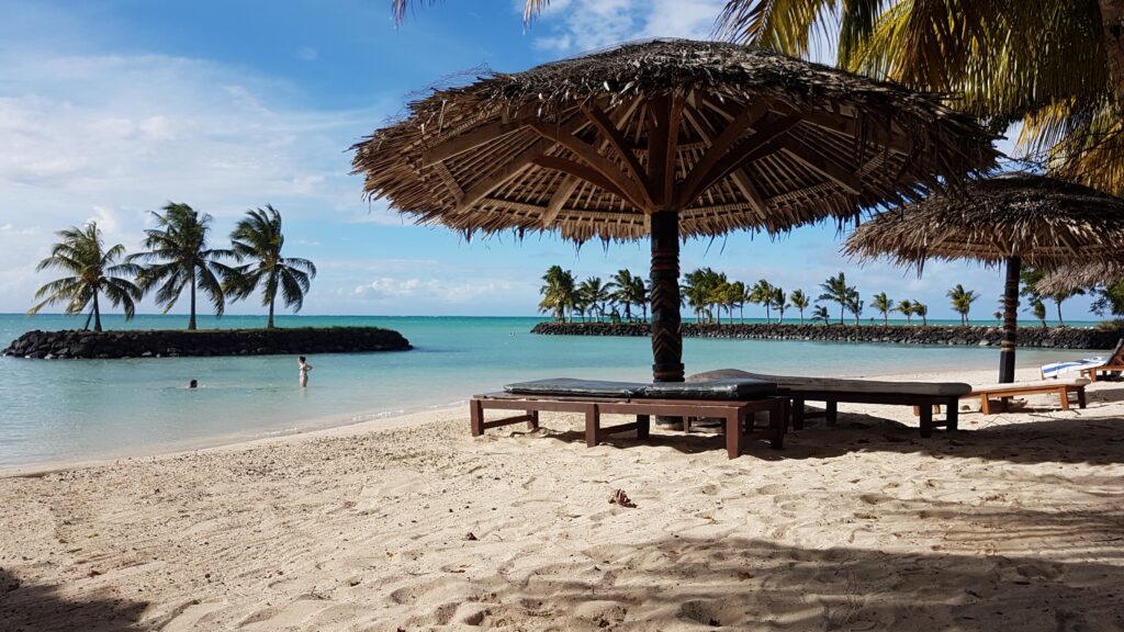 A photo of the beach outside the Sheraton hotel in Samoa, with palm trees and naturally made beach chairs and umbrellas