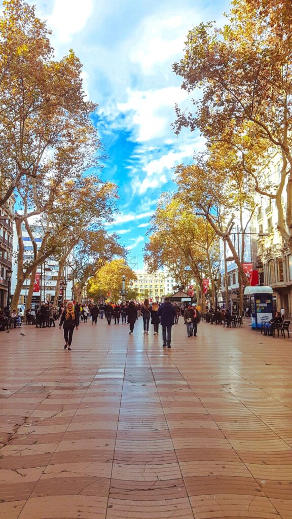 The busy La Rambla street filled with people, shops and trees on either side