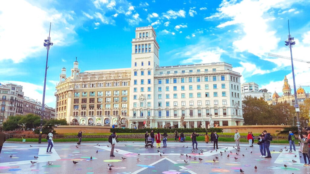 Plaça de Catalunya filled with people and pigeons.