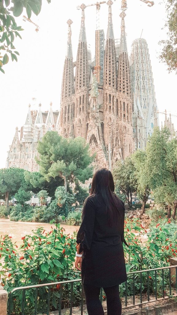 A woman looking at Sagrada Familia from across the pond surrounded by trees