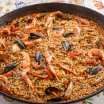 A large round dish consisting of rice of seafood paella toped with prawns, mussels and clams