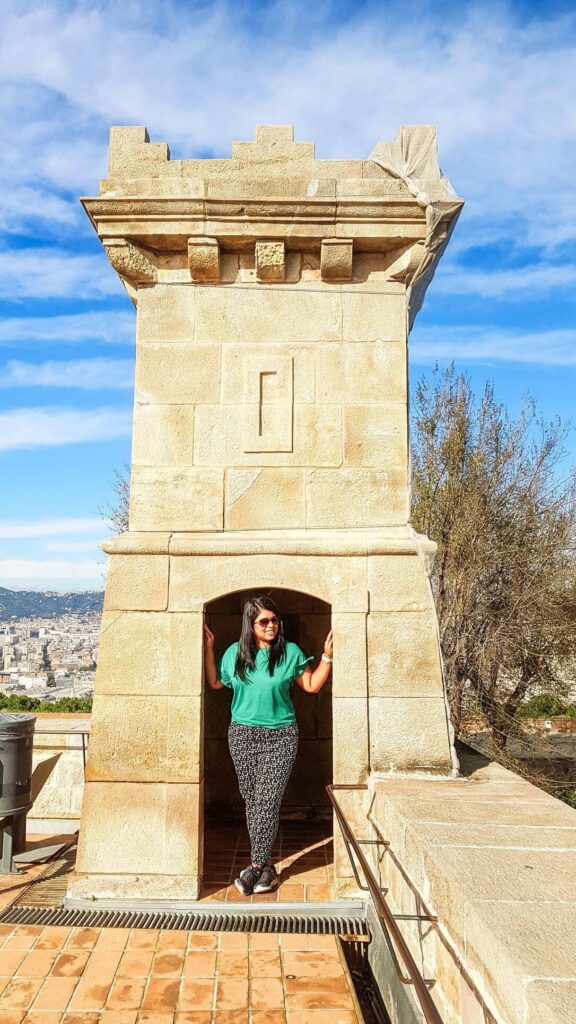 Concrete brown structure on top of a castle with an entranceway infront of which there is a girl standing. Beautiful blue skies on a bright sunny morning