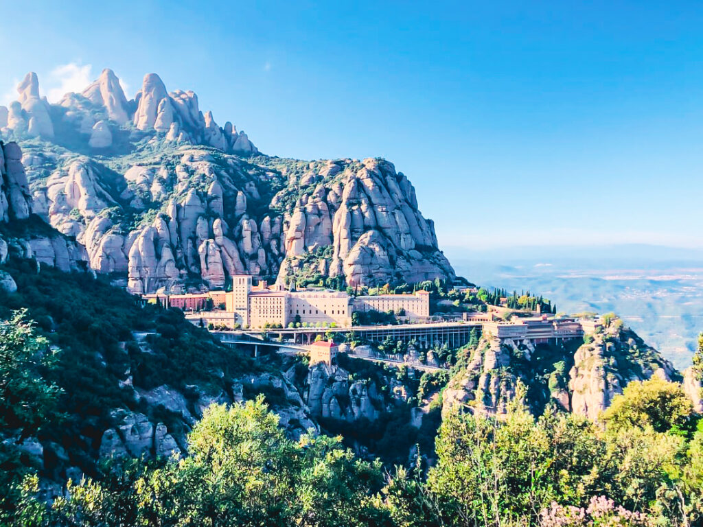 A front on view of Montserrat and the saw tooth like mountains up on a hill surrounded by green trees.