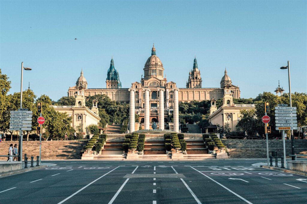 White concrete building referred to as Museu Nacional D'art De Catalunya sitting at the end of a wide concrete road.