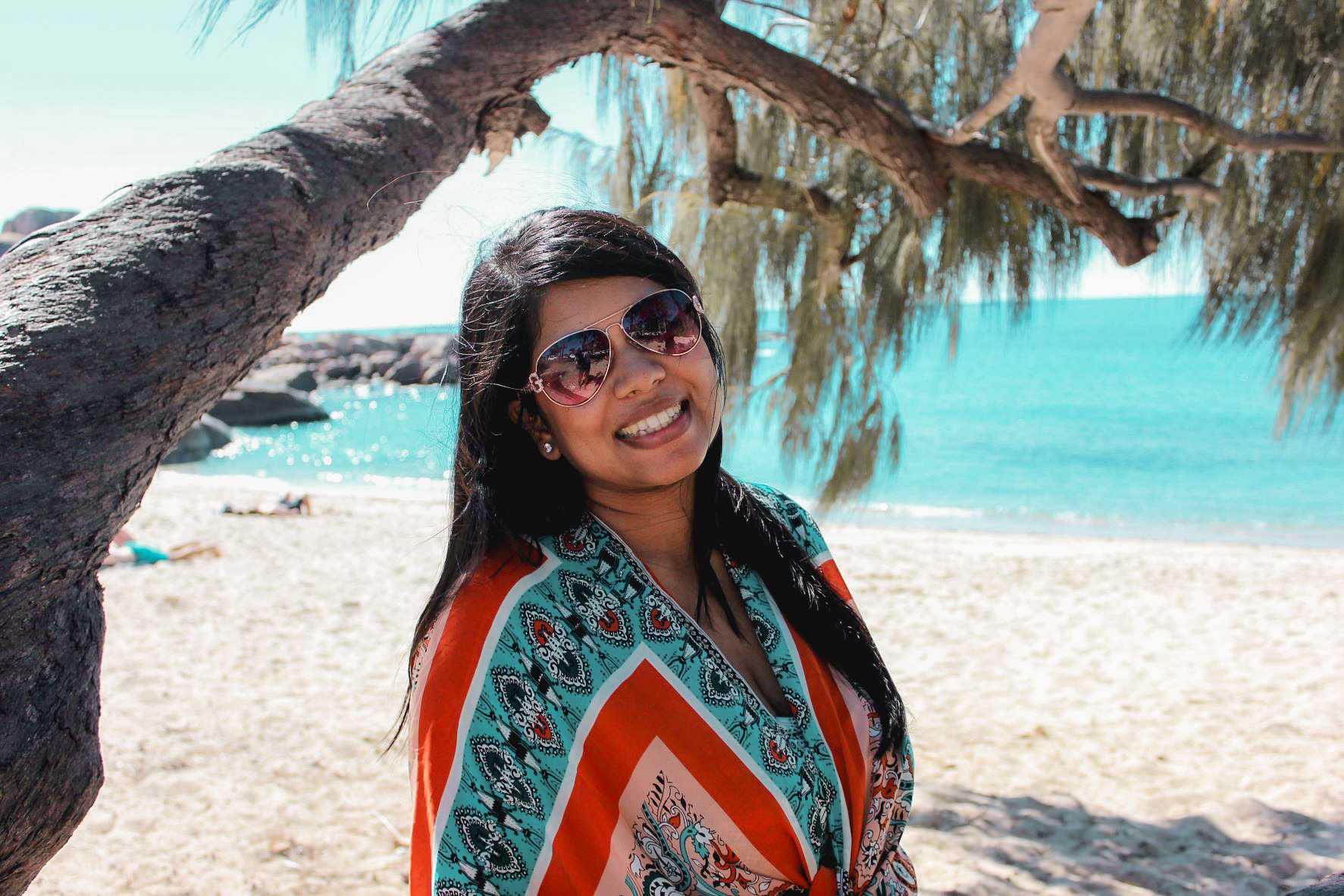 Photo of a woman standing at a beautiful beach infront of a tree