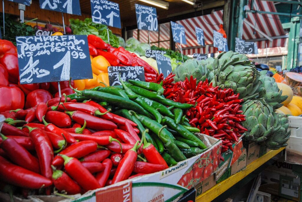 A phot of a stall at Naschmarkt with bright red and green chillis, artichokes, yellow and red peppers and price boards.