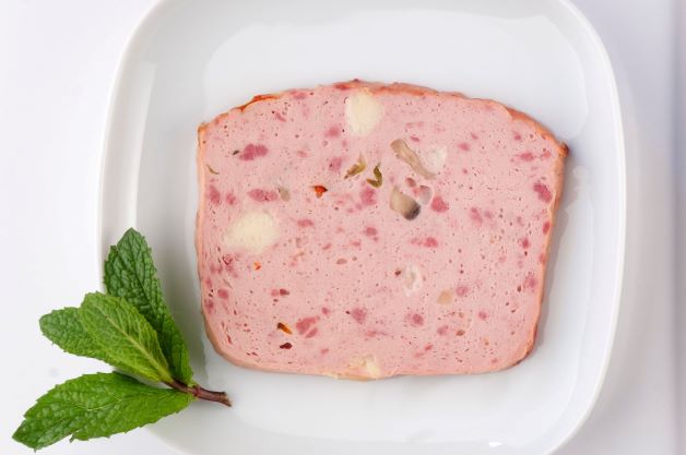 A slice of spam, cut and laid out on a plate with some mint leaves on the side for garnish.