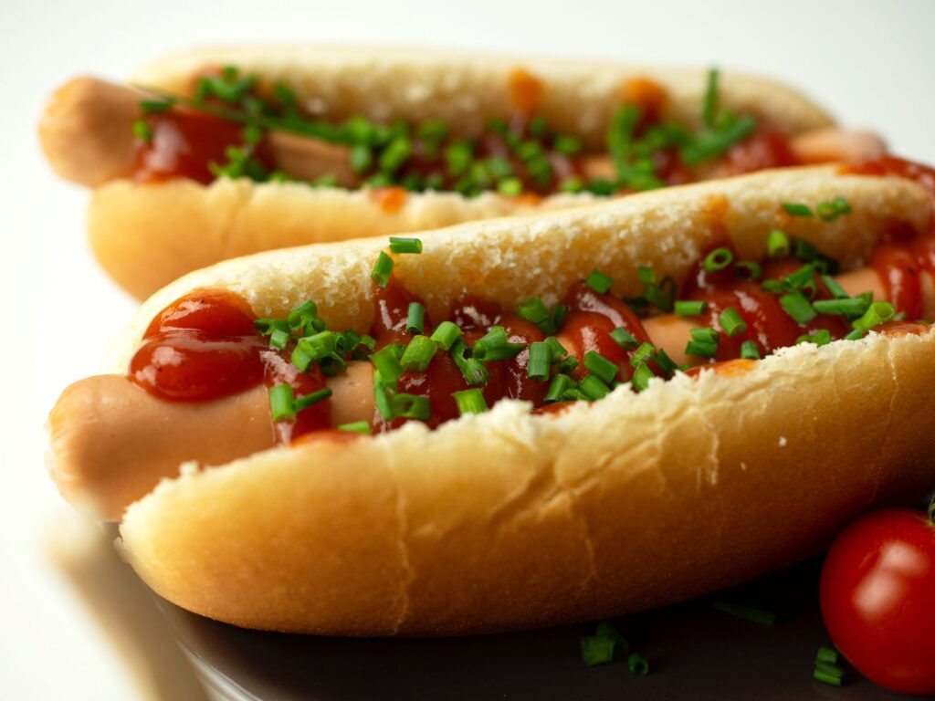 A saussge inside a hot dog bread roll topped with sauce and garnished with fresh chives
