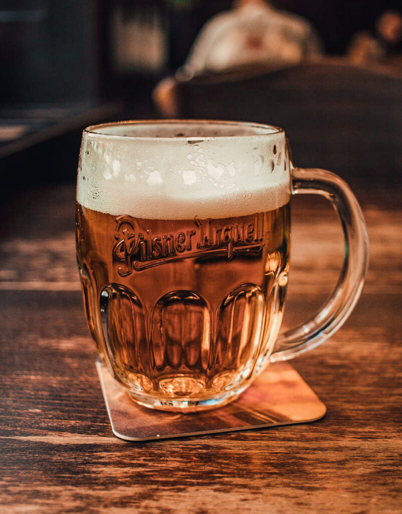 A glass of Czech Beer laid on a coaster sitting on a wooden table