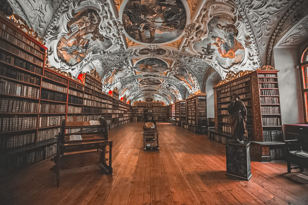 A picture of the Strahov Library with its beautiful ceilings filled with artwork and a display of an extensive collection of books.