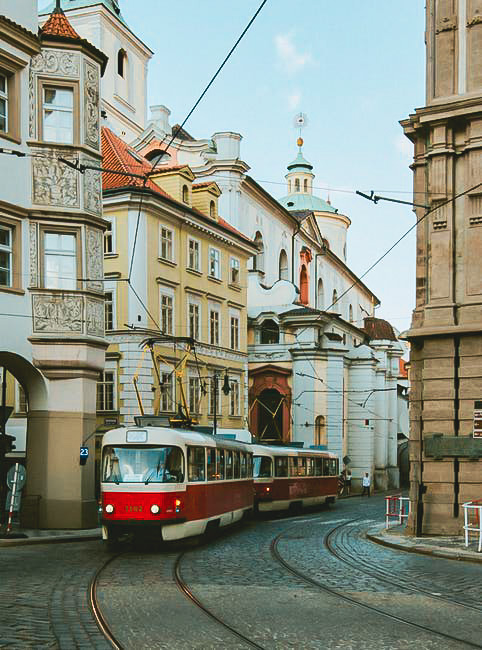 A picture of Tram 23 passing through the streets of Prague among some historic buildings.