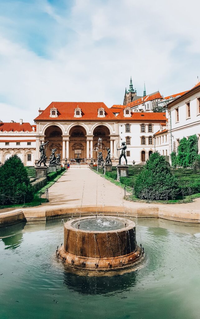 A photo of the beautiful Wallenstein Gardens with the Palace at the far end and a pond and fountain surrounded by lush greenery.