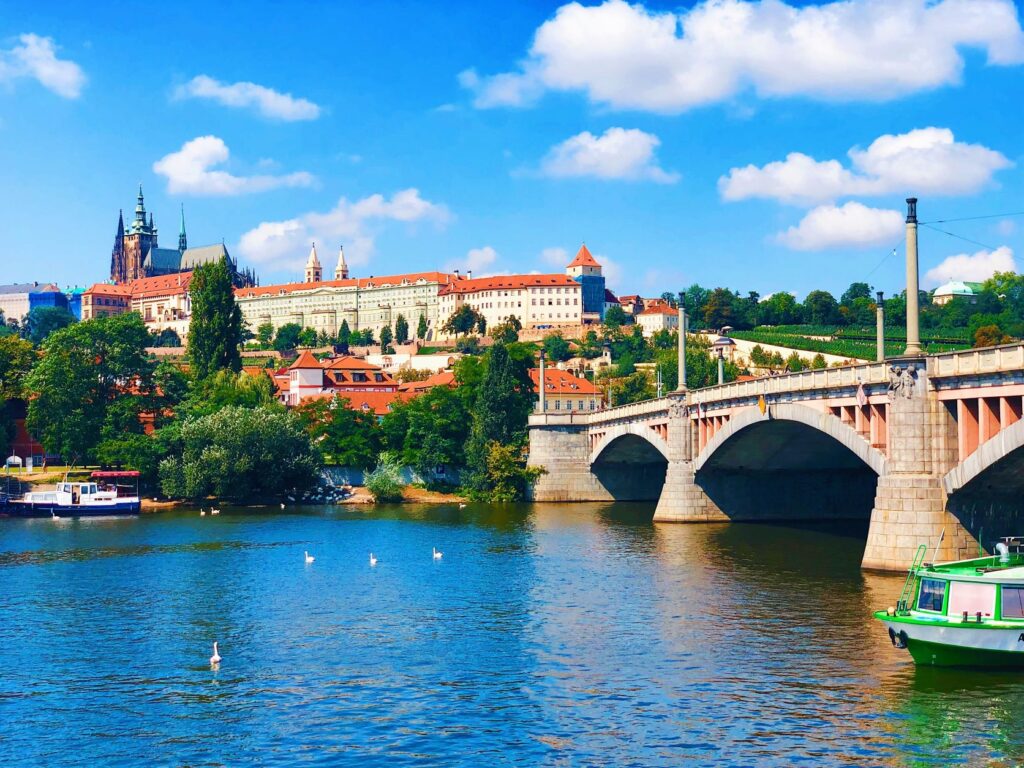 An image of the River Vlata showcasing Charles Bridge and A beautiful view of Prague castle and its grounds in the distance.