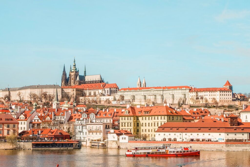 A beautiful photo of Prague Castle and the neighborhood as well as a boat cruising down the River Vltava