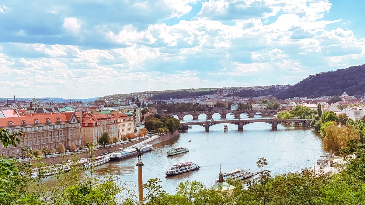 An arial view of bridges across the river with orange tiled houses on either side of the river and green trees surrounding them