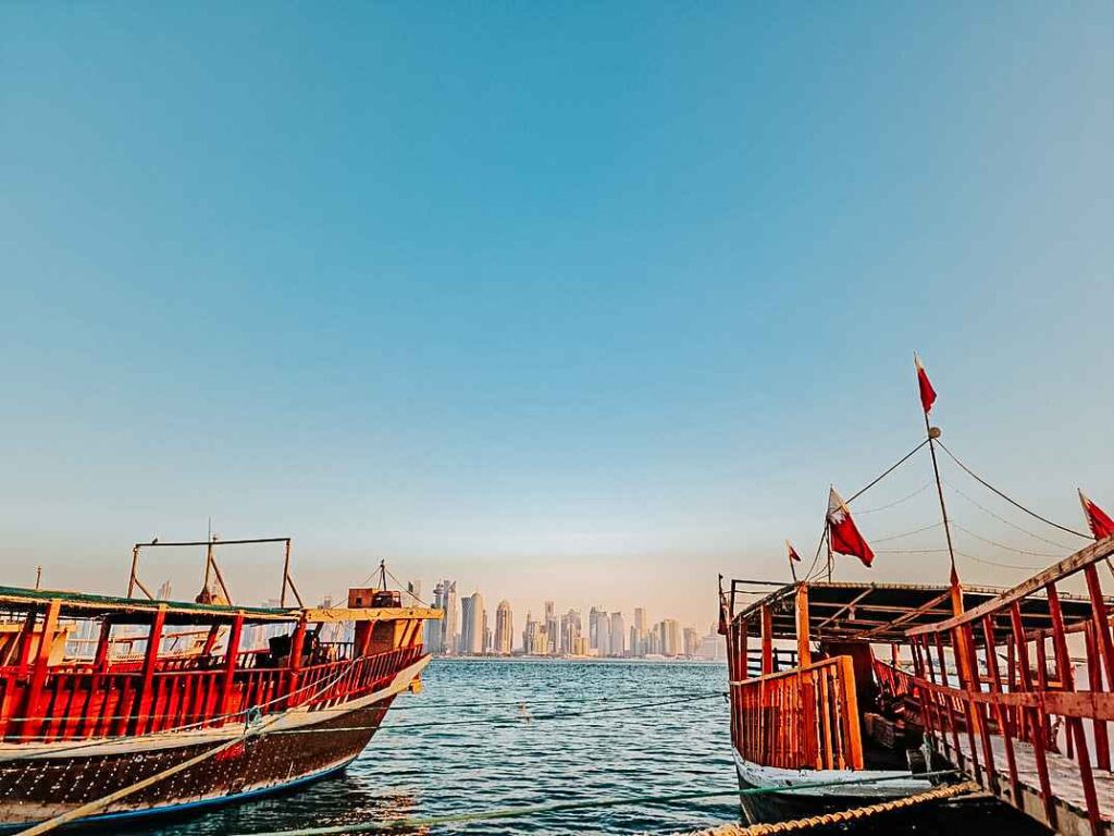 Two wooden boats sitting atop of the water with buildings in a distance