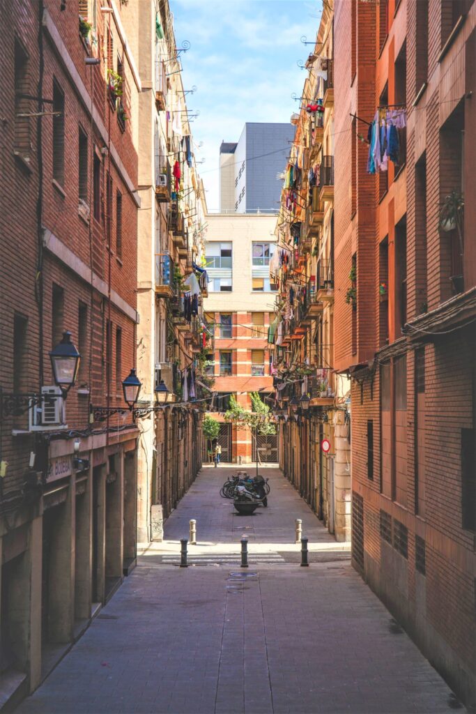 a narrow street in barcelona with concrete buildings on either side and clothes hanging off balconies