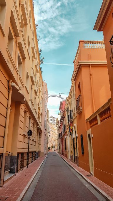 A picture of old town Monaco with a narrow street and cobblestone sidewalk  that sits between buildings on either side