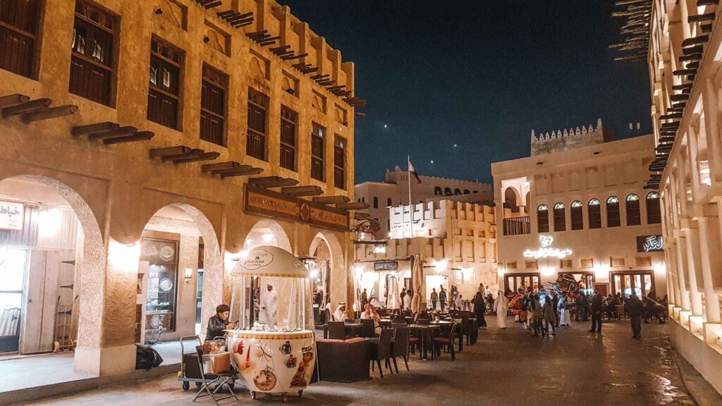 Brown concrete buildings all around, fully light up, with stalls and people walking through the market.A must visit place during your 3 days in Doha.