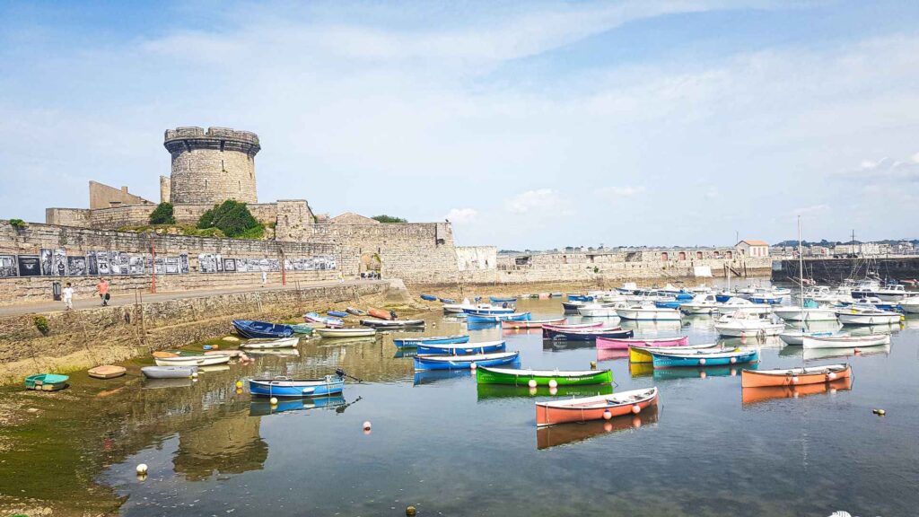 calm body of water with red, blue. yellow, green, pink boats with a brown structure in the background