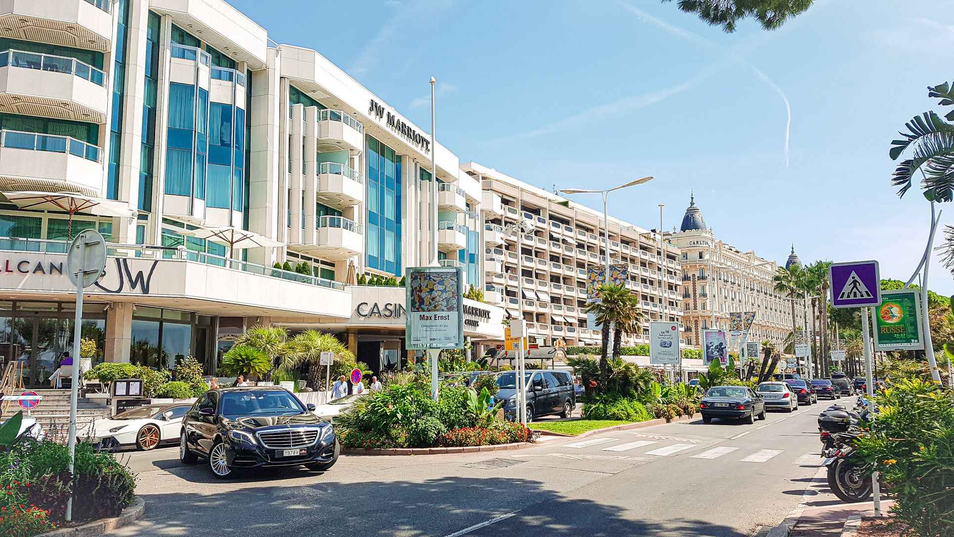 a street filled with concrete white fancy buildings and fancy cars and bikes