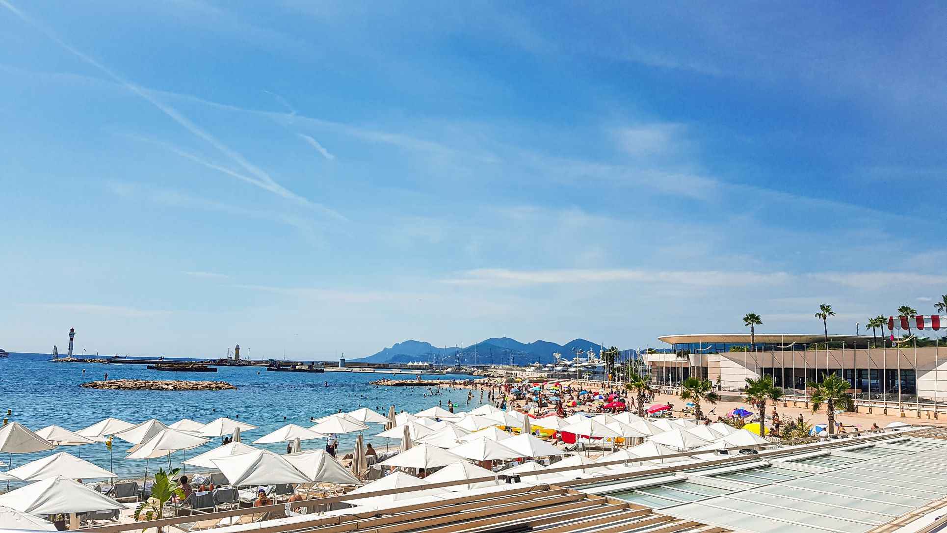 beautiful beach with clear blue waters and white top umbrellas on the golden sand where people are sunbathing all during a bright sunny day