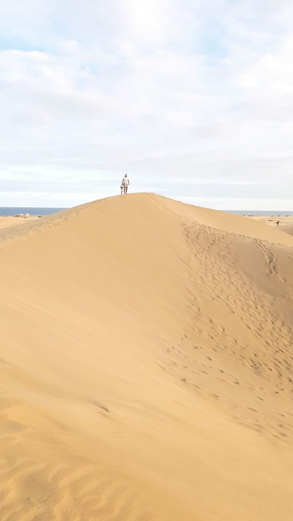 mountains of sand with a man and child standing on a peak in the distance