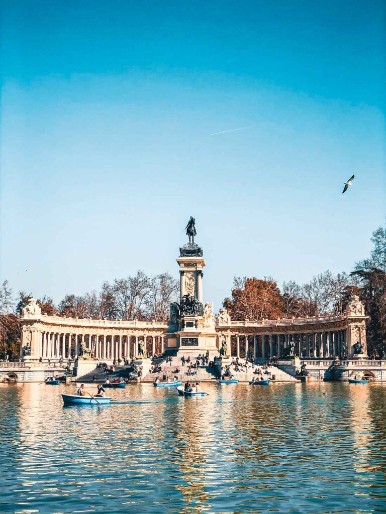 beautiful concrete monument facing the lake with boats in the water and people rowing from one end to another