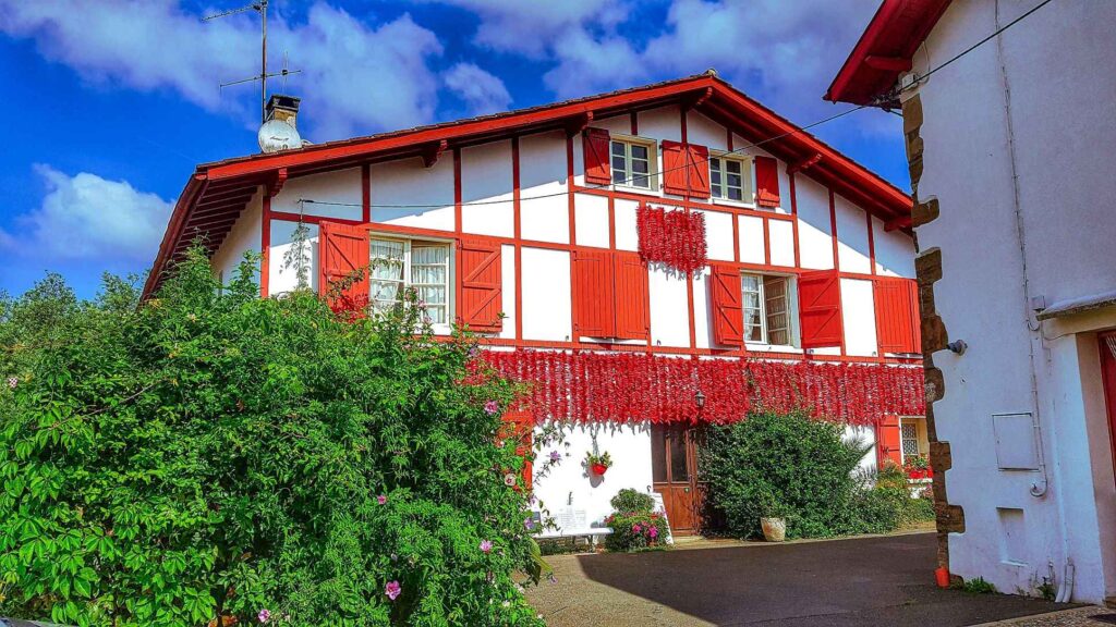 white house with red roof and red windows with red chillis handing off the house and green trees in front of it