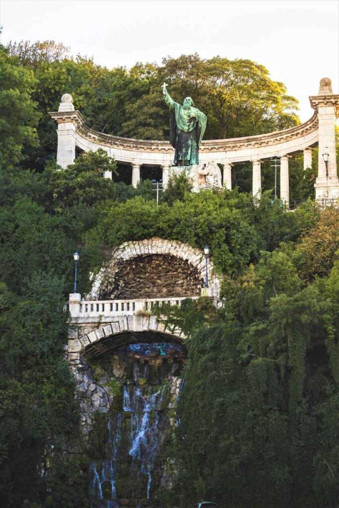 statue near waterfall and green plants during day time