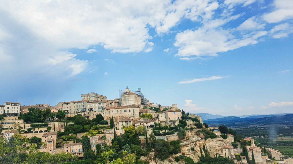 Hilltop with whitewashed houses and green trees under the bright blue sky. One of the top places to visit in the south of france