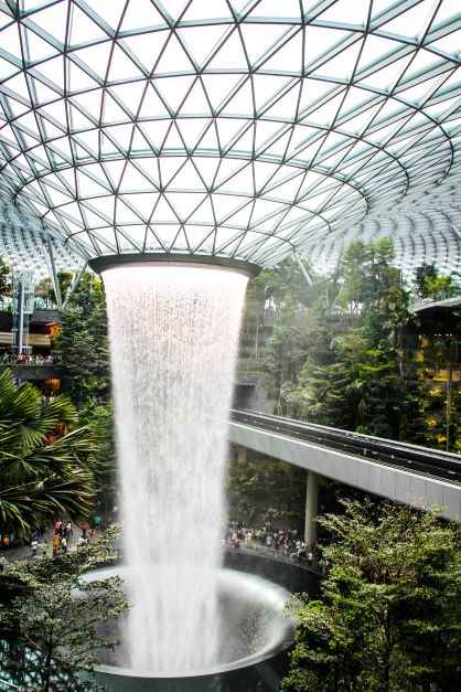 large water fountain inside building surrounded by green trees. Surprisingly One of the top Singapore attractions not to be missed