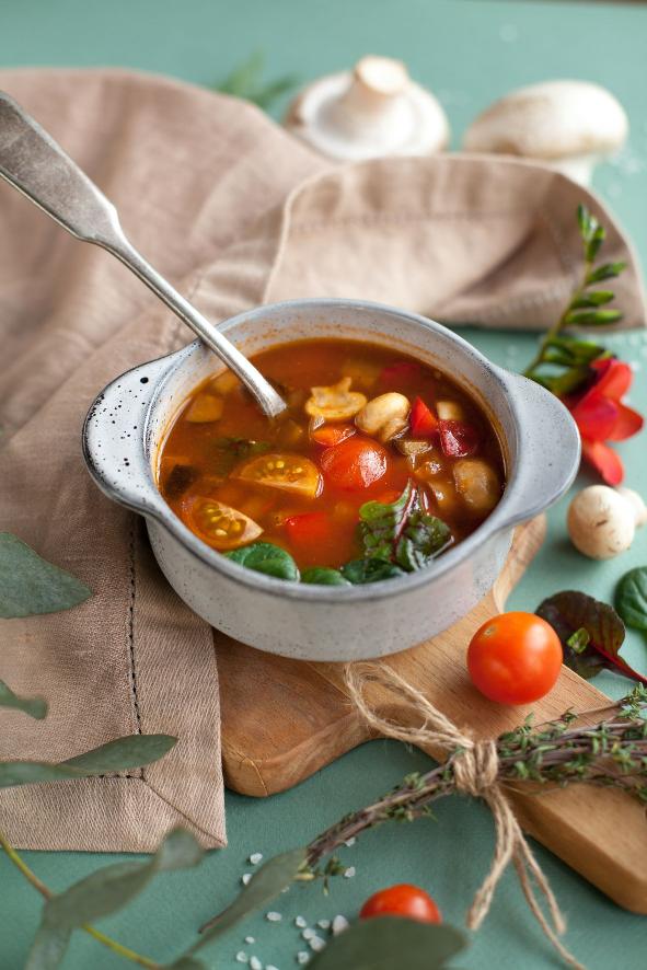 white bowl with soup and vegetables sitting on a beige cloth with tomatoes all around