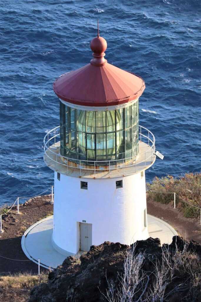 white and red lighthouse sitting on the corner of a cliff overlooking the ocean. one of the top places to visit in Oahu