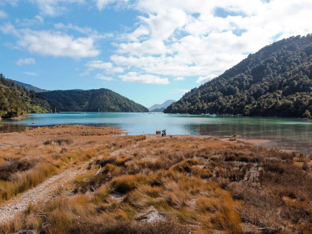 brown grass, blue lake and green mountains with people standing on the grass