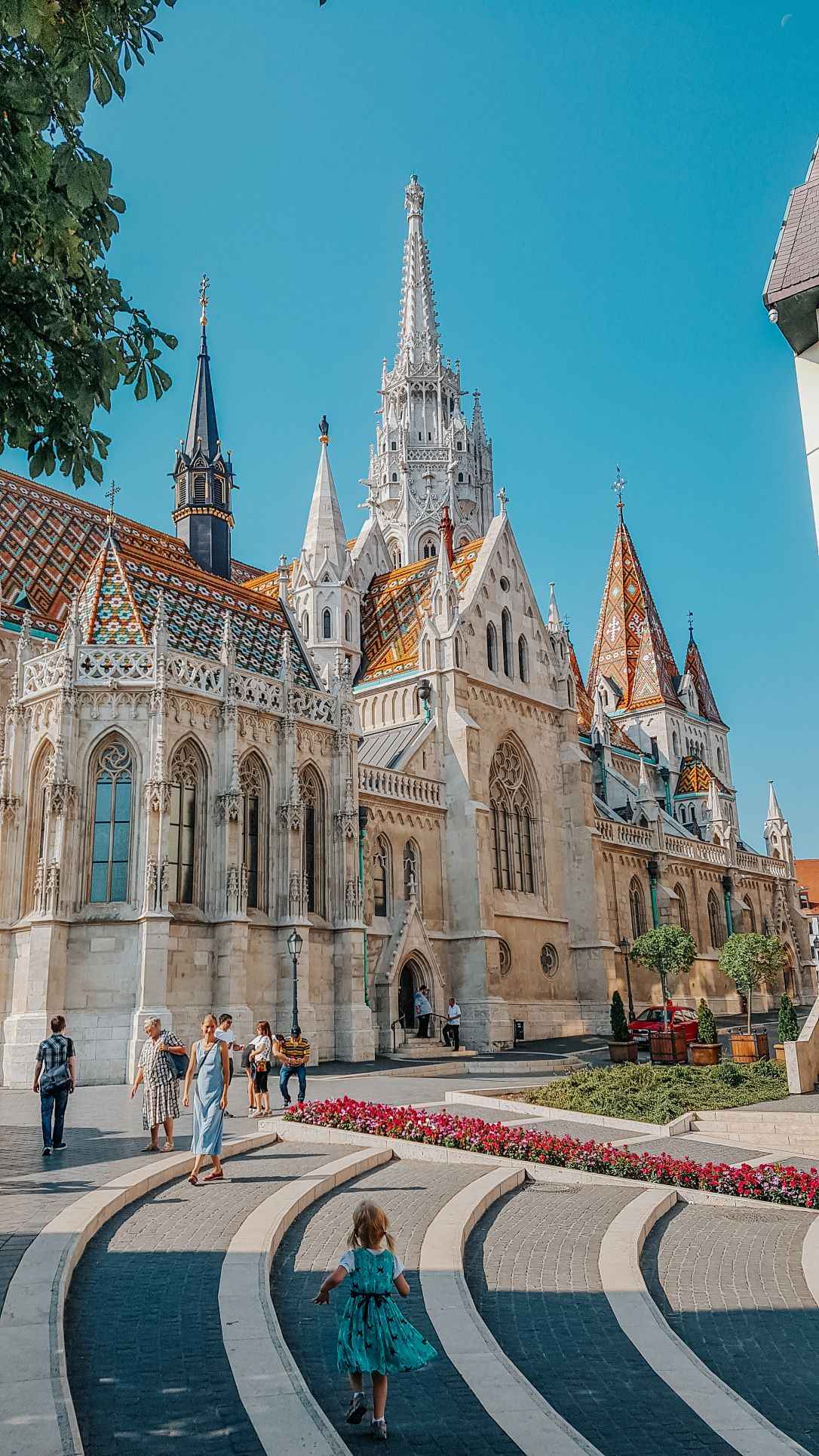 beige cathedral with orange and blue tiled roof and intricate work done through it during day time with people walking around