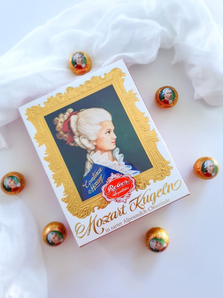 Box with a photo of a lady and six balls of chocolate laying on the outside around a white cloth