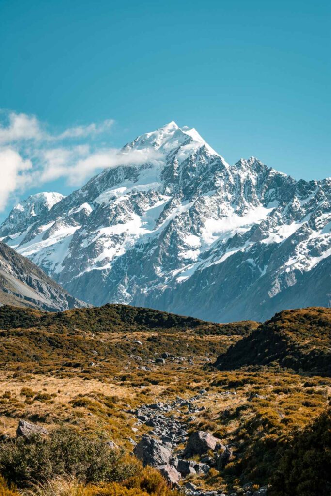 snow capped mountain sitting behind brown and green grass. Undeniably one of the top attractions in New Zealand