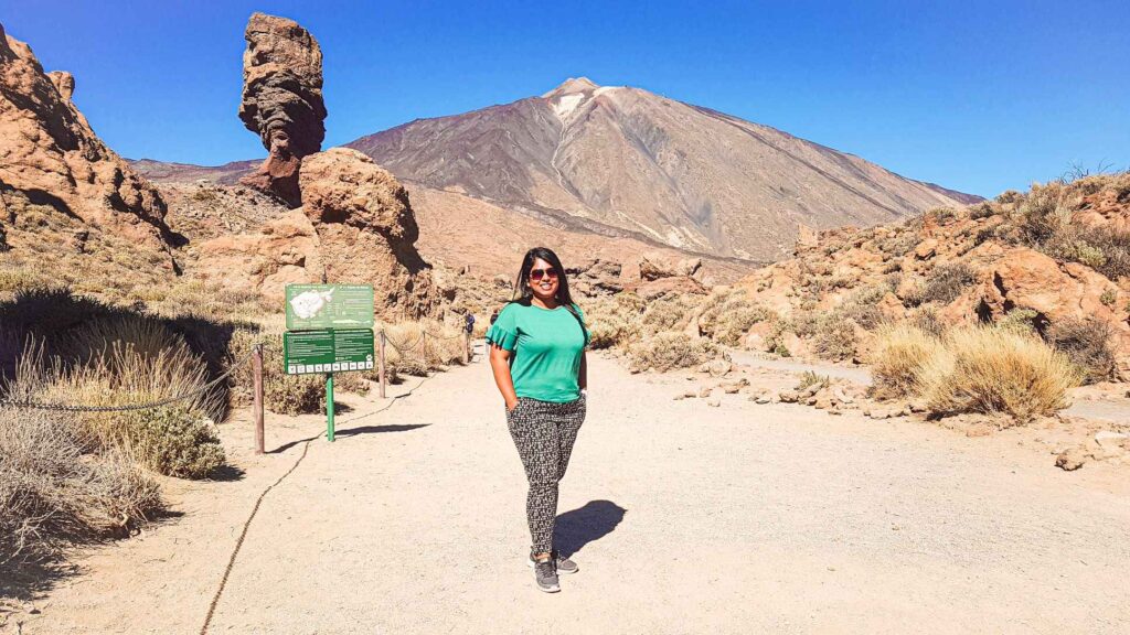 picture of a girl standing in a dessert infront of rocks and a large mountain