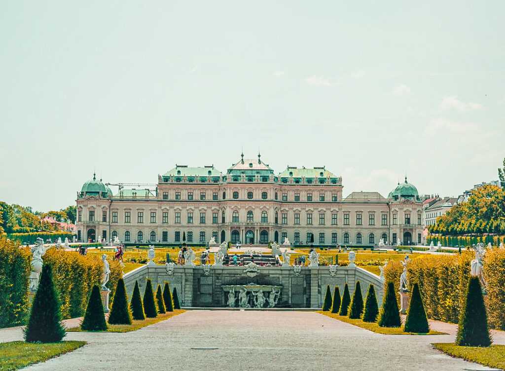 beautiful white palace with green roof in a massive garden with green and yellow trees.