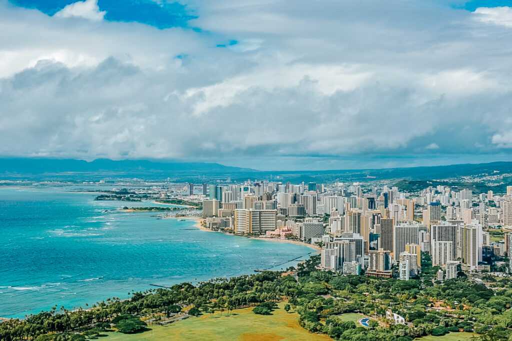 Arial view of city with concrete tall buildings on one side and ocean on the other surrounded by green mountains during daytime