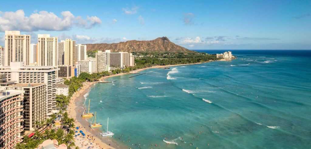 View looking out to a beach with golden sand and blue waters surrounded by concrete tall buildings during daytime