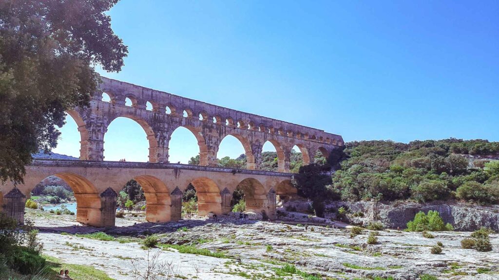 brown concrete bridge with archways running through it and trees on either side. One of the top places to visit in the south of france