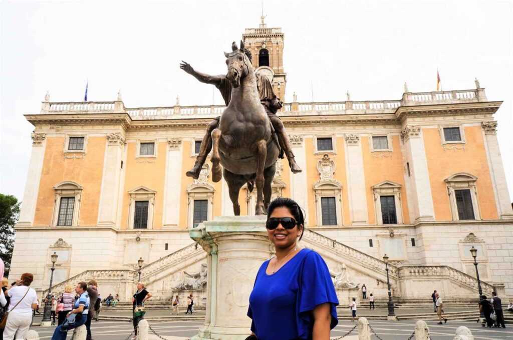 girl standing in front of statue of a man on a horse infront of a concrete building during day time