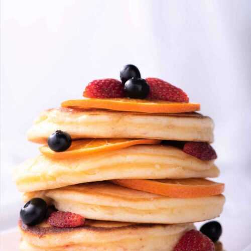 Stack of fluffy pancakes on a plate with red and black fruits scattered around