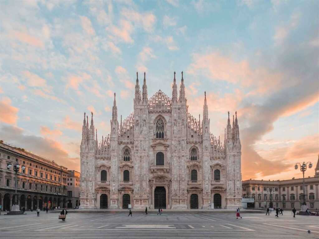 White concrete church during dawn with people walking infront of it. Waking up early on holiday is one of the top travel tips for any traveler.