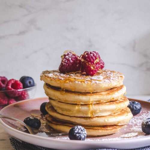 Thick pancakes stacked on a plate topped with fruits