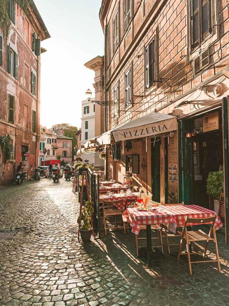 cobblestone street with shops on either side and tables and chairs on the sidewalk during daytime