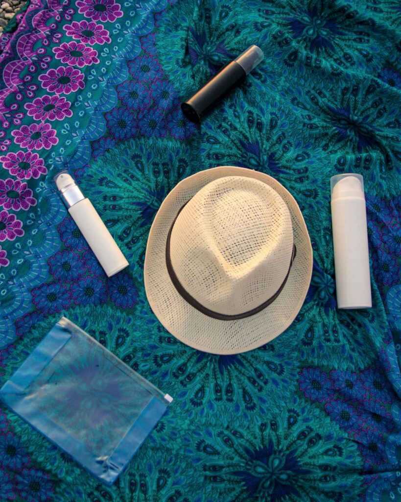 hat and bottles of sunscreen on a colorful mat. One of my top travel tips when traveling anywhere